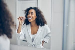 Cheerful young woman with a toothbrush in her hand looking at herself in the mirror